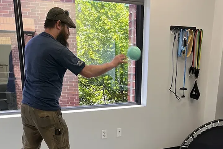 Patient working through a return-to-function ball drill in the therapy gym