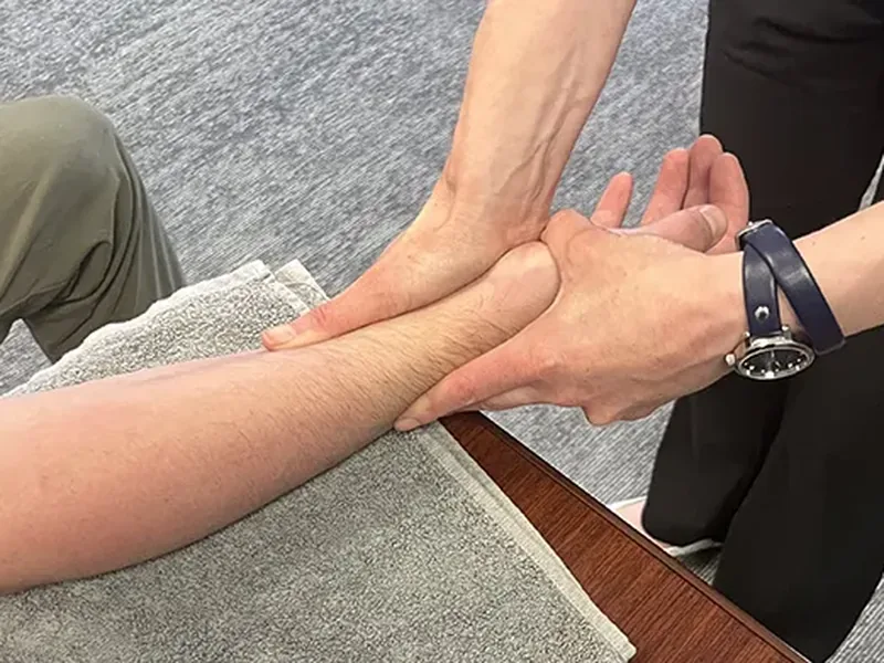 Therapist performing hands-on soft tissue work on a patient&rsquo;s forearm