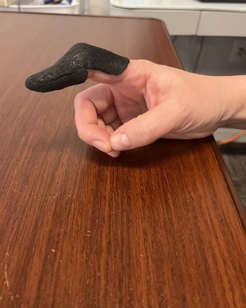 Black custom molded finger splint fitted over the index finger, hand resting on a wooden desk