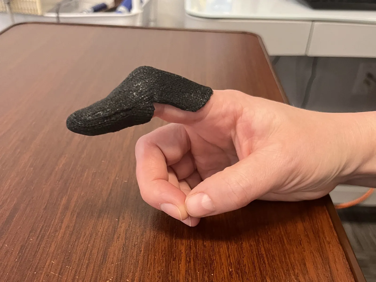 Black custom molded finger splint fitted over the index finger, hand resting on a wooden desk