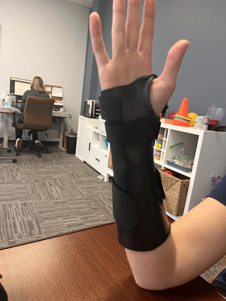Black custom molded forearm and wrist splint with hook and loop straps, worn with the fingers and thumb free