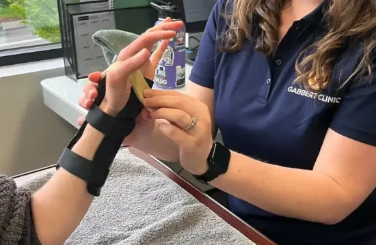 Gabbert Clinic therapist fitting a black custom molded wrist and hand splint on a patient seated at a treatment table