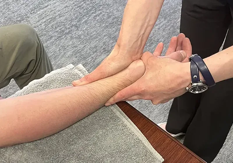 Therapist performing hands-on soft tissue work on a patient's forearm