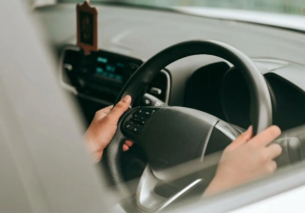 Driver&rsquo;s hands holding a car steering wheel, seen from over the shoulder